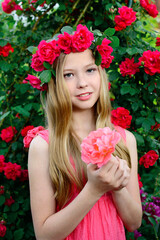 Obraz na płótnie Canvas Portrait of a young beautiful girl with curly blond hair in a flower wreath on a background of roses. Beauty and fashion concept