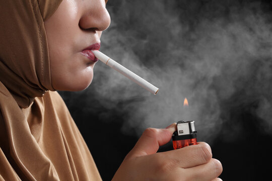 Close up young muslim woman smoking a cigarette on black background