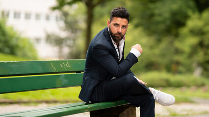 Obraz premium Young gorgeous man sitting on bench in a park, outdoor - outside