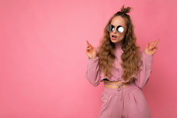 Attractive sexy self-confident young blonde woman wearing everyday stylish clothes and modern sunglasses isolated on colorful background wall looking to the side