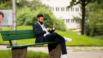 Fototapeta premium Young businessman sitting on a bench using his cell phone