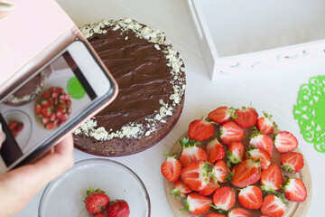 The woman takes pictures of the cooking process. Chocolate cake with peanuts and strawberries.