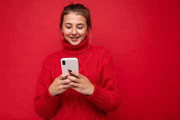 Beautiful young woman wearing casual clothes standing isolated over background surfing on the internet via phone looking at mobile screen