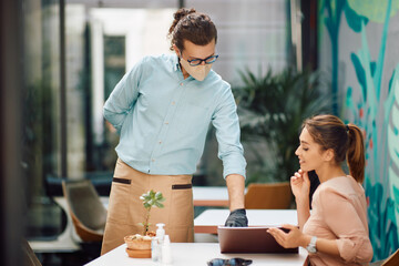 Waiter with face mask helping his guest to choose an order from a menu at restaurant.