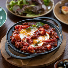 Frying pan with hearty breakfast. Fried eggs with tomatoes and minced meat at table.