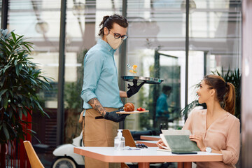 Happy waiter wearing protective face mask while serving young woman in a cafe.