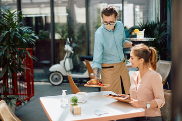 Happy woman enjoying while waiter is serving her at reopened restaurant during coronavirus pandemic.