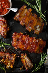 Overhead view of barbecue smoked ribs with red sauce on black surface