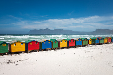 Famous colorful beach houses in Muizenberg near Cape Town, South Africa with mountains of Cape of Good Hope Peninsula in the background.