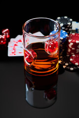 Casino chips, playing cards, glass of whiskey and dices on dark reflective background