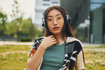 Listens to the music in headphones. Young asian woman is outdoors at daytime