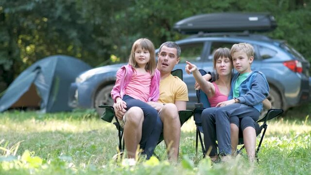 Happy young family parents and kids sitting together at campsite in summer talking happily together.