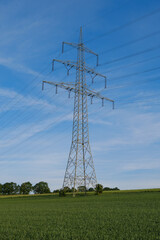 Hochspannungsmast / Stromleitung steht in einer Landschaft unter blauen Himmel im Hochformat