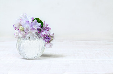 A small bouquet of lilac flowers in a glass vase on a white wooden table