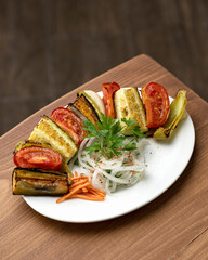 Plate of vegetables. Baked eggplant with tomatoes and bell peppers on wooden background. Vertical format. Soft focus. Copy space.