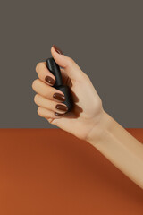 Beautiful groomed womans hand with trendy autumn nail design on brown background