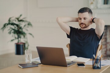 Male entrepreneur looking at laptop screen and relaxing while working in modern office