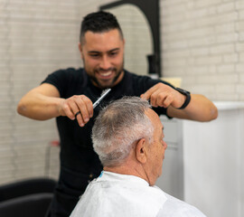 Obraz na płótnie Canvas Barber enjoys cutting hair with scissors for senior client at barbershop