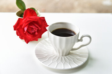 A cup of black coffee and a red rose on a white table