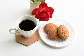 A cup of black coffee on a stand, cookies and a red rose on a white background