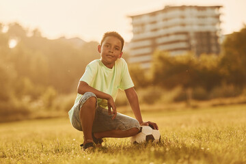 Taking a break. With soccer ball. African american kid have fun in the field at summer daytime
