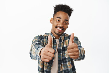 Happy and positive african american man showing thumbs up, smiling satisfied, praise excellent great job, say yes, compliment you, encourage, standing over white background - obrazy, fototapety, plakaty