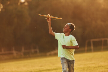 Running with toy plane. African american kid have fun in the field at summer daytime