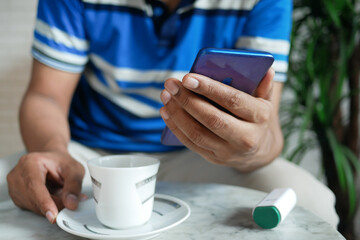 young man hand using smart phone and drinking tea while sited on a chair 