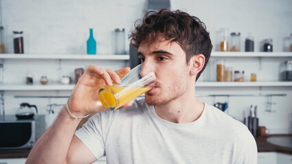 man in white t-shirt drinking refreshing orange juice in morning