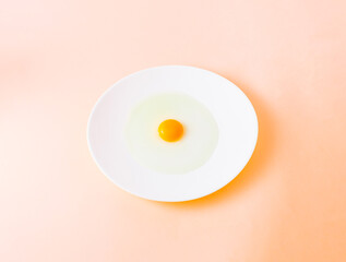 Fresh chicken egg on a white plate with egg white and egg yolk. Pastel beige background. Flat lay. Minimal concept.