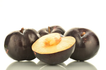 Three whole and one half sweet tasty dark purple plums, close-up, isolated on white.
