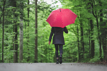Frau mit rotem Regenschirm auf Waldweg