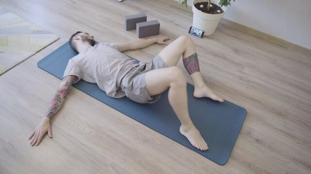 Young man relaxing and doing reclined spinal twist yoga pose at home