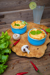 Pots with mushroom julienne on a wooden board, decorated with herbs. Julienne in cocotte with yellow cheese crust.