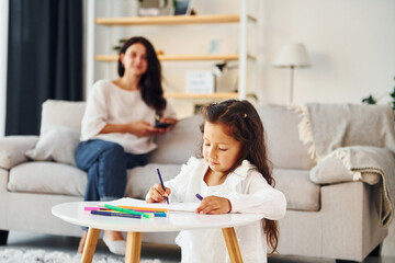 Girls is painting. Mother and her daughter spending time together at home