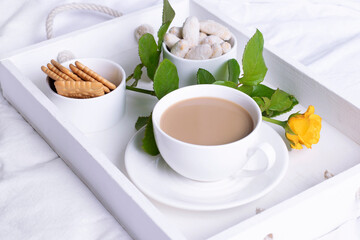 Morning coffee in a white tray on a white bed close-up.
