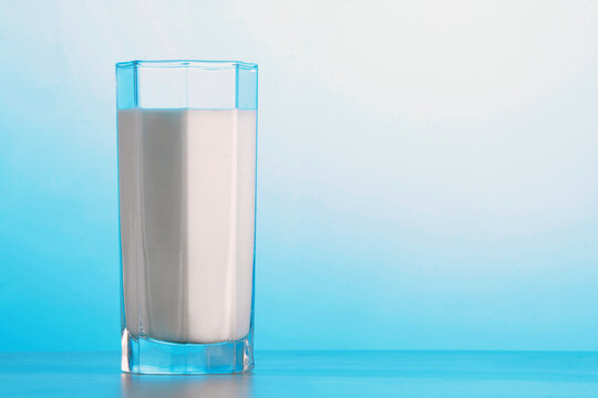Milch im eckigen Trinkglas vor Hintergrund in blau mit Textfreiraum rechts