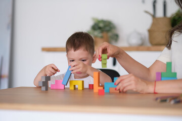 kid boy and mother playing educational toys at table at home. child's playing with colorful wooden bricks at the table.