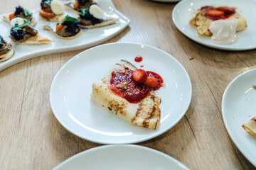 Pancakes with strawberry jam, catering table. Other dishes in the background.
