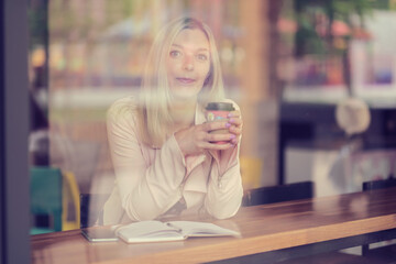woman in the cafe sits at a table, drinks coffee and looking away. vintage color tone