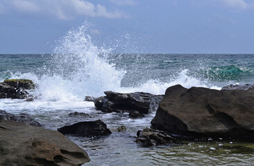View from the rocky coast to the sea, splashes from the waves, large stones in the foreground