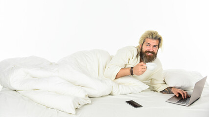 Fototapeta premium Social networks dependence. Morning coffee routine. Social media. Modern life. Screen Time and Insomnia. Happy hipster drink coffee in bed. Bearded man enjoy coffee and surfing internet laptop