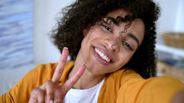 Cute beautiful joyful curly-haired African American woman, student, freelancer, posing for selfie on smartphone, fooling around, having fun, looking at phone camera, smiling happily
