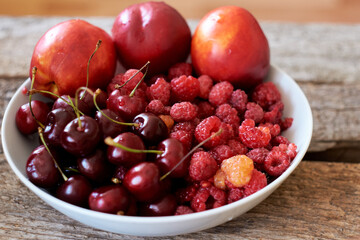 red berries and fruits in a plate on a wooden background