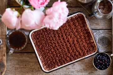 Homemade tiramisu. Peonies, coffee, blueberries. Wooden background. Top view.