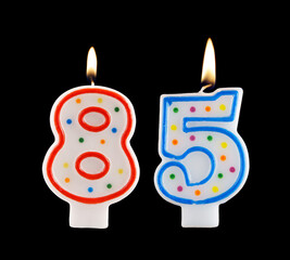 Burning birthday candles isolated on black background, number 85