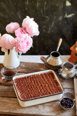 Homemade tiramisu. Peonies, coffee, blueberries. Grey and white background. Side view.