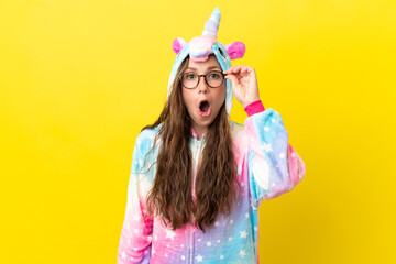 Girl with unicorn pajamas over isolated background with glasses and surprised