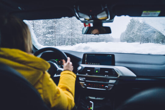 Cropped image of female driver sitting near helm in car transporting on wild snowy environment, back view of woman looking at snowy road travel by car having insurance in trip