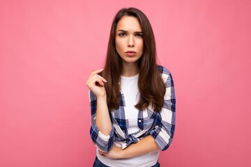 Shot of youngsad dissatisfied beautiful brunette woman with sincere emotions wearing trendy check shirt isolated on pink background with empty space and having doubts